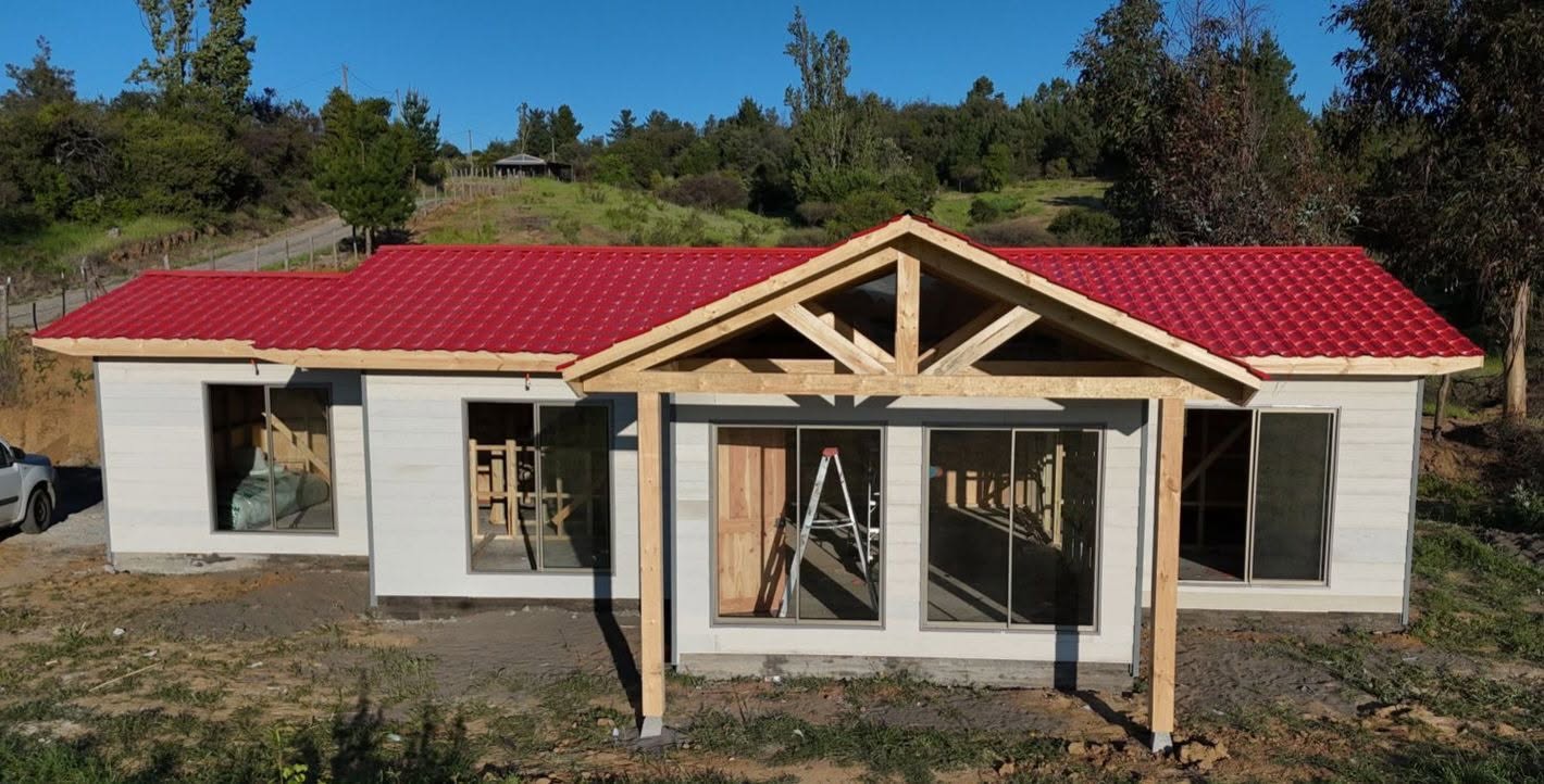 Casa de madera construida por Fuzam, con techo rojo y acceso con vigas a la vista
